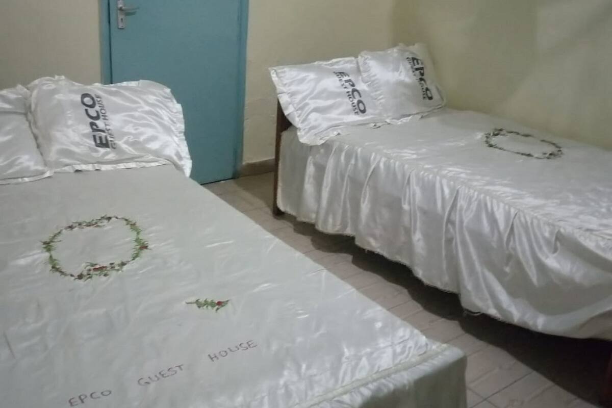Two single beds with white bedding and pillows labeled 'EPCO GUEST HOUSE'.
