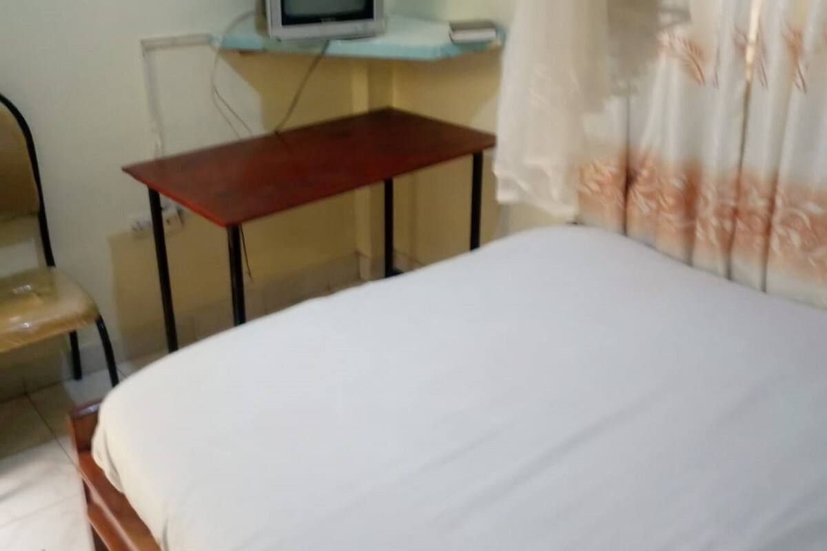 A bedroom with a bed, a desk with a television, a chair, and a curtain.