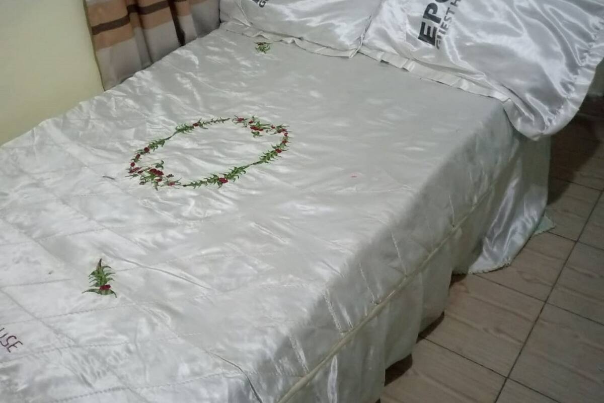 A bed with a white bedspread and pillows labeled "EPCO GUEST HOUSE".