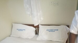 A bed with two pillows labeled "EPCO GUEST HOUSE NAIVASHA" and a plain white bedspread. - Epco Guest House (Naivasha)
