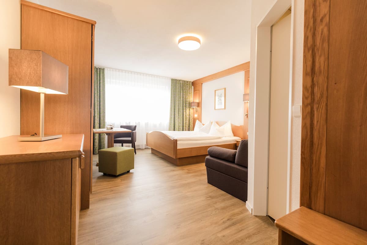 A hotel room with a bed, a desk, a sofa, and a lamp.