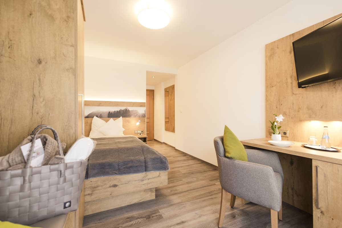 A hotel room with a wooden bed, a desk with a chair, a television, and a small table with a vase and a bottle.