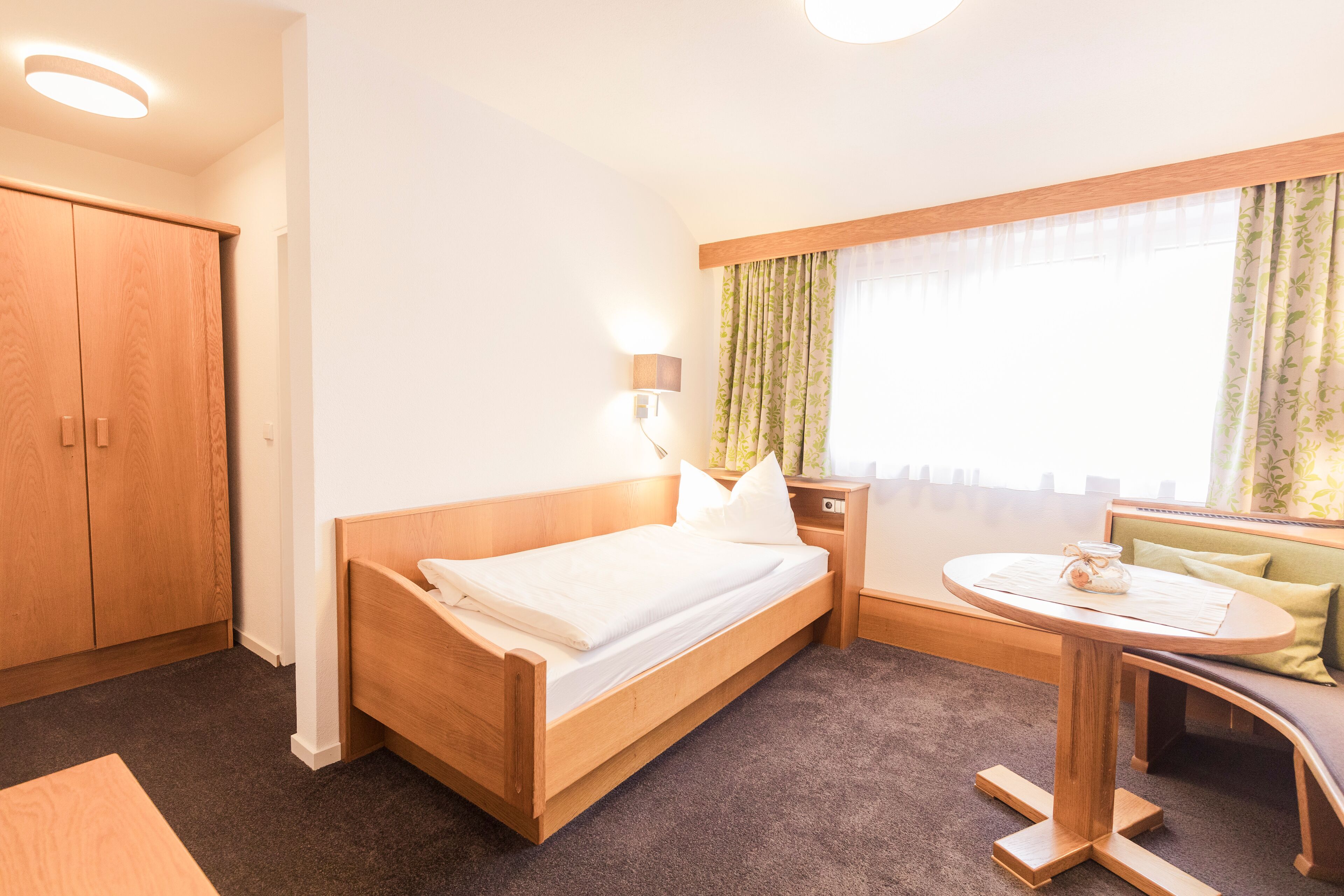 A hotel room with a wooden bed, a small round table, a green sofa, and a window with curtains.