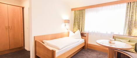 A hotel room with a wooden bed, a small round table, a green sofa, and a window with curtains.