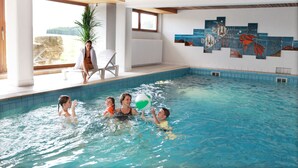 Piscina interna com um mural na parede, um vaso de planta e uma área de estar com cadeiras.