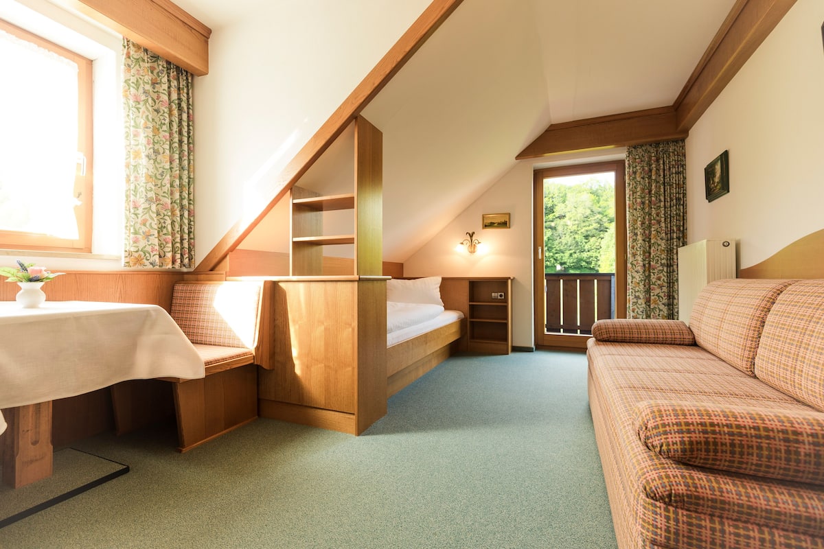 A cozy room with a bed, a sofa, a small table, and a window with curtains.