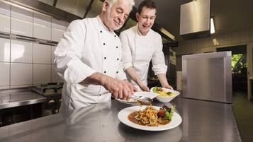 Two chefs in a modern kitchen with stainless steel appliances and a clean, organized layout.