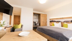 Quarto de hotel moderno com cama, televisão, secretária de madeira e vista para as montanhas.