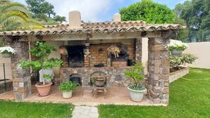 A stone-built outdoor kitchen with a brick fireplace, surrounded by potted plants and a stone wall.