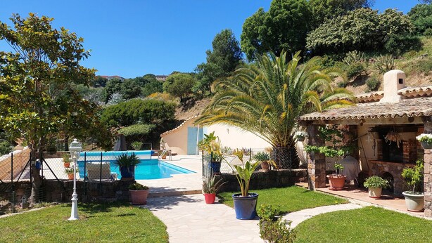 A villa with a swimming pool, stone patio, and lush garden.
