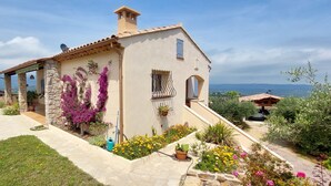 A Mediterranean-style house with a stone facade, a tiled roof, and a garden with flowering plants and potted plants.
