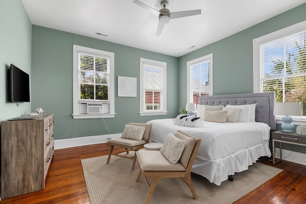 A bedroom with a bed, two chairs, a TV, and a desk.