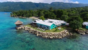 A turquoise building with a thatched-roof structure nearby, surrounded by clear blue waters and lush greenery. - Luna Sea Inn Ocean view (Bluefields)