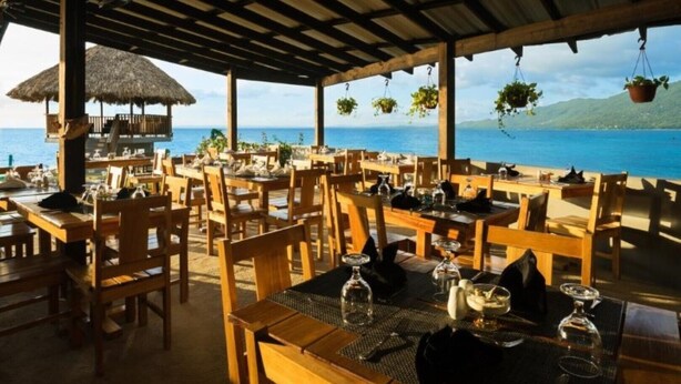 An outdoor restaurant with wooden tables and chairs, a thatched-roof structure, and hanging plants. - Luna Sea Inn Ocean view (Bluefields)