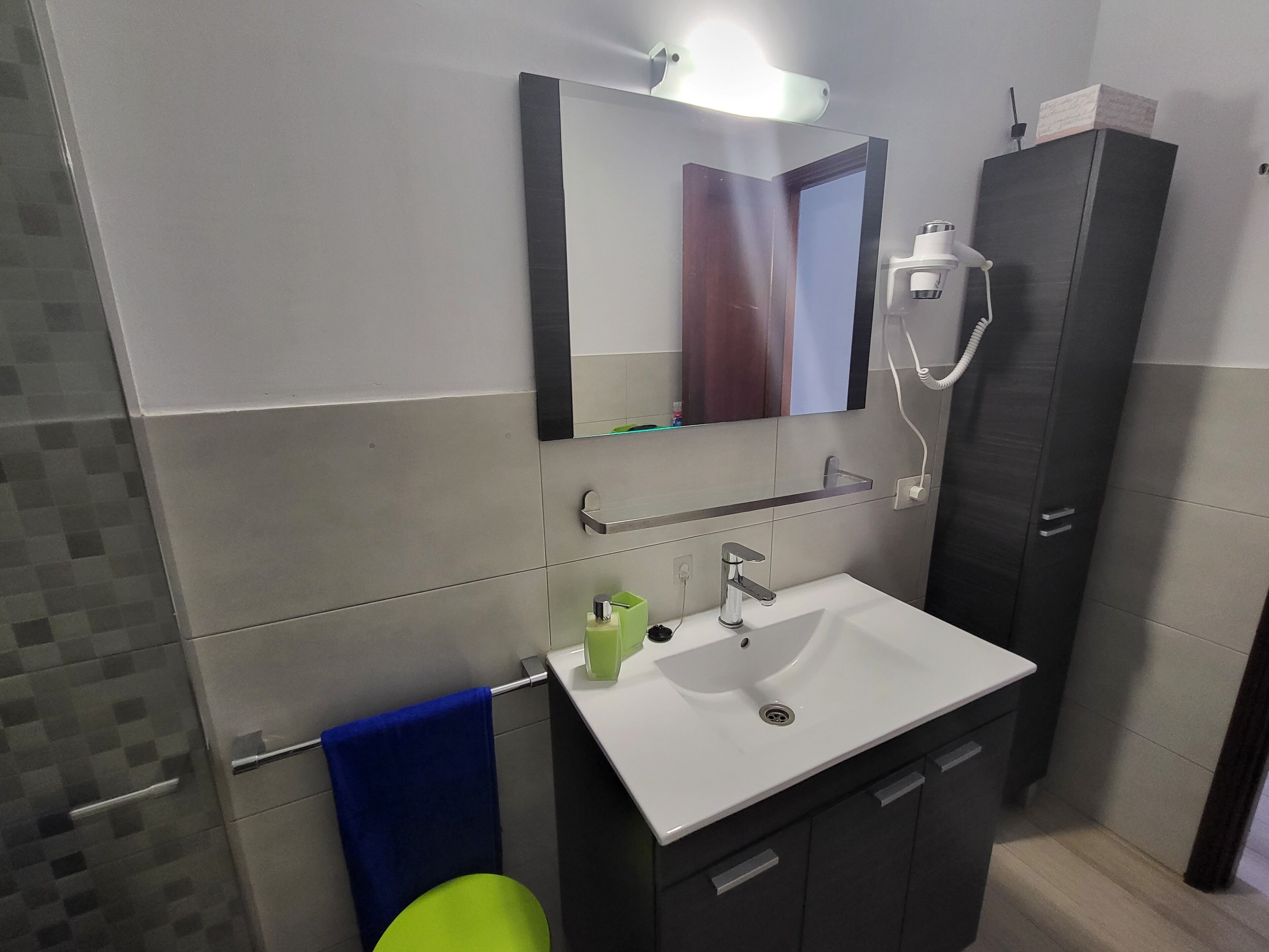 A modern bathroom with a white sink, a mirror, a towel rack, and a dark cabinet.