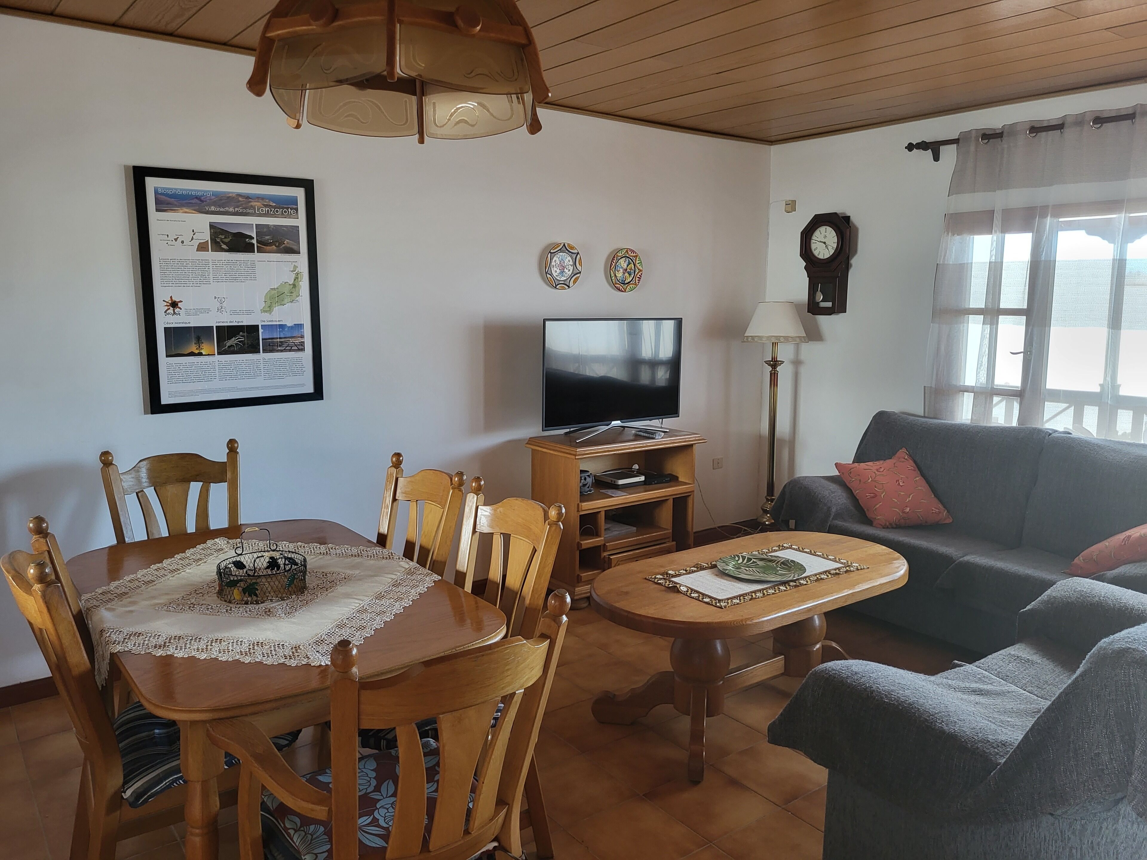 A cozy living room with a wooden dining table, chairs, a television, a sofa, and a lamp.