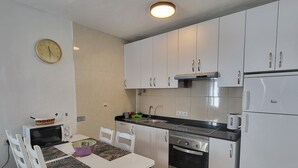 Una cocina compacta con gabinetes blancos, microondas, estufa y pileta.