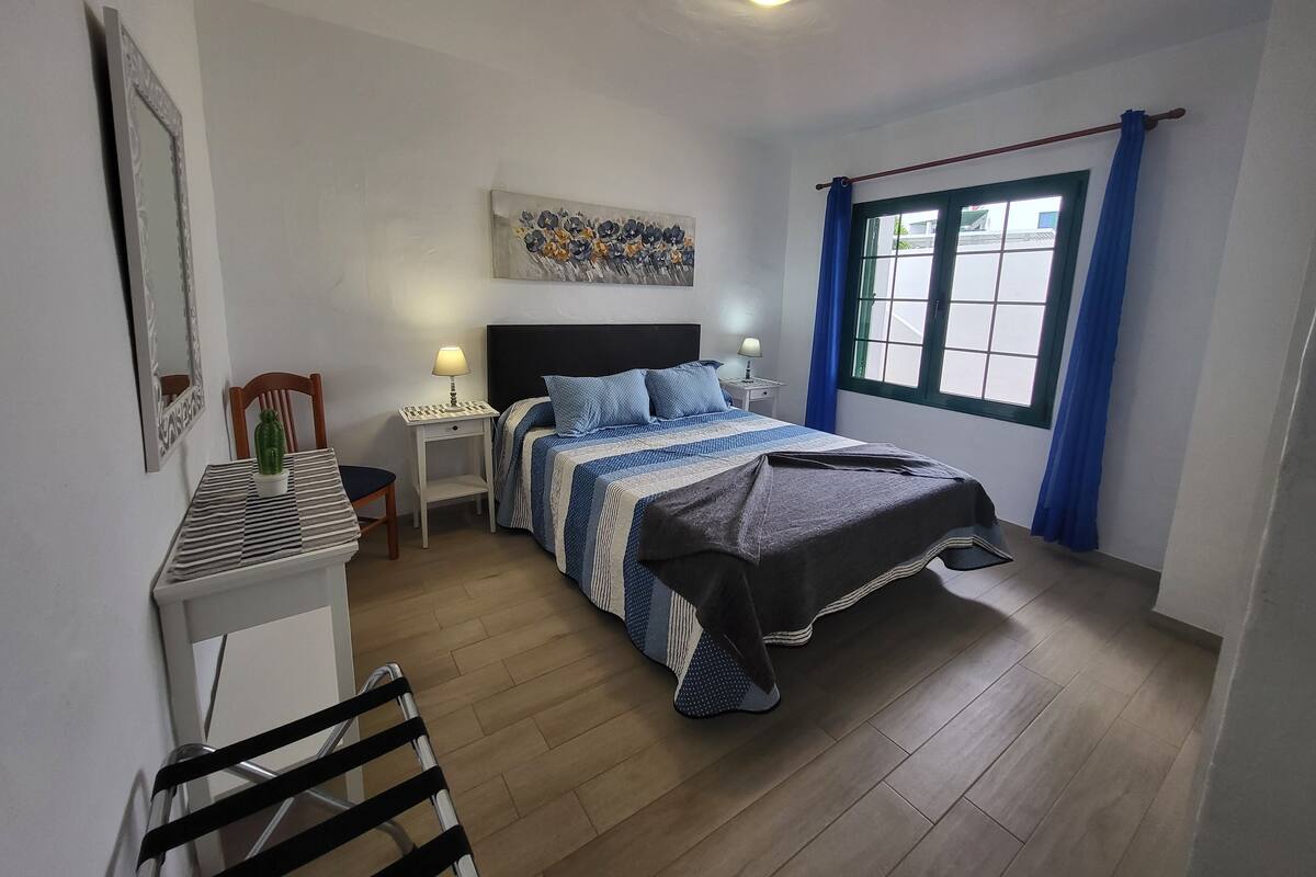 A bedroom with a bed, bedside tables, a chair, a desk, a window with curtains, and a ceiling light.