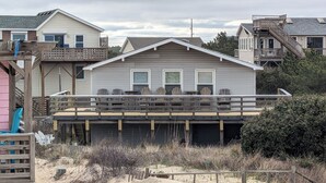 Une maison située en bord de mer, dotée d’une terrasse couverte, d’une jetée en bois et d’une plage de sable au premier plan.