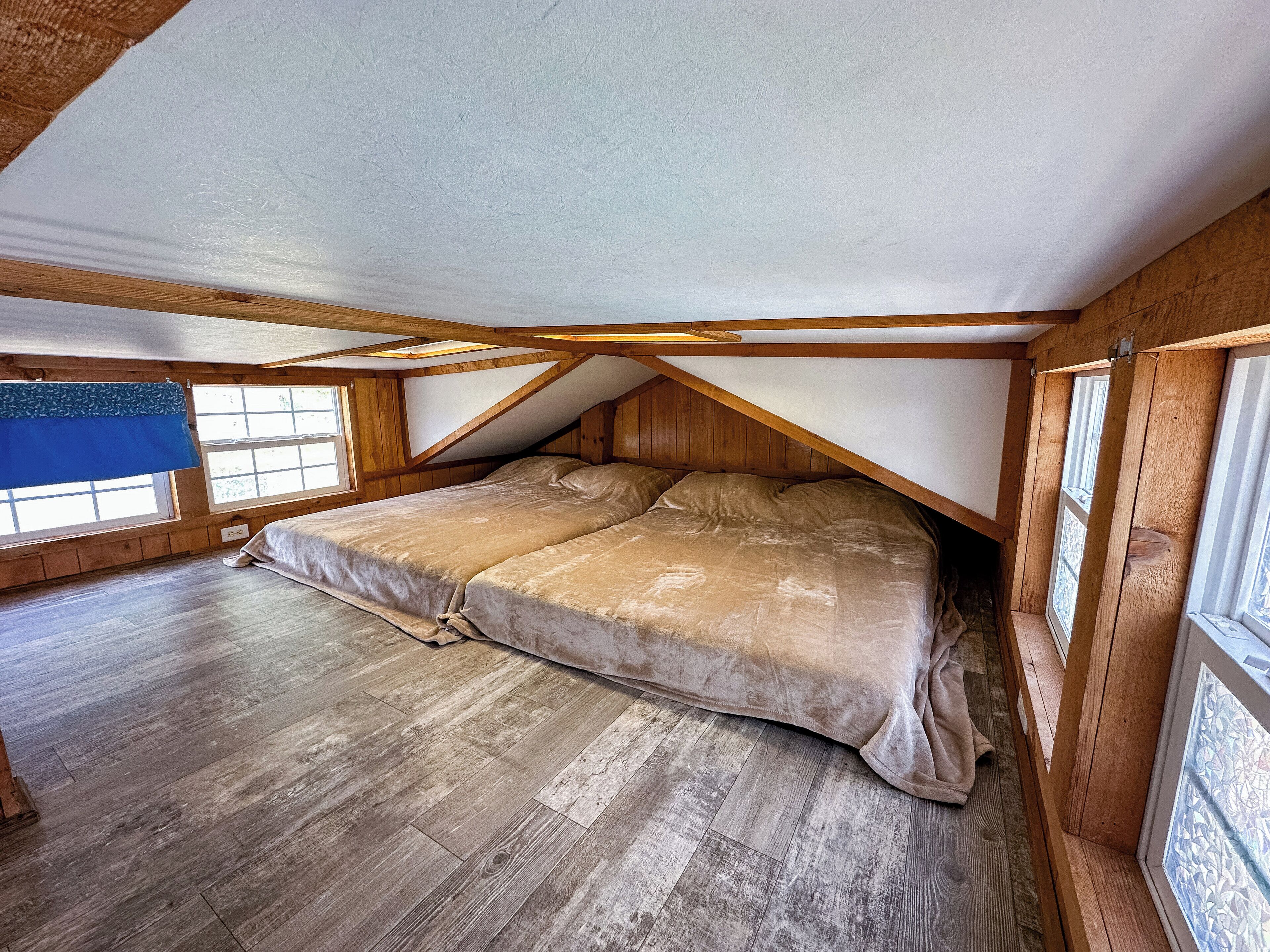 A bedroom with a loft-style bed, wooden beams, and large windows.