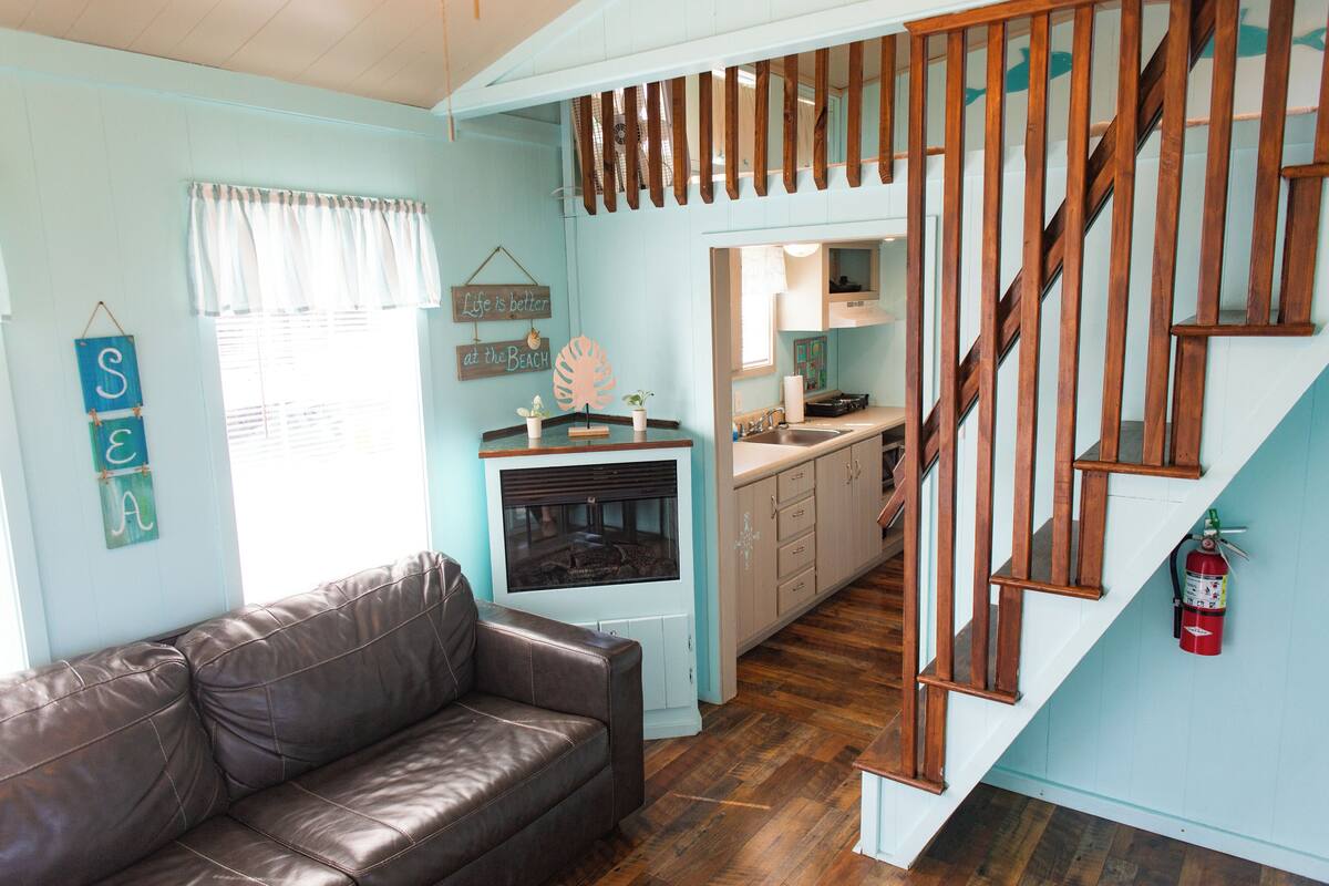 Un salon chaleureux avec un canapé en cuir marron, une cuisine dotée de meubles en bois et un escalier avec des rampes en bois.