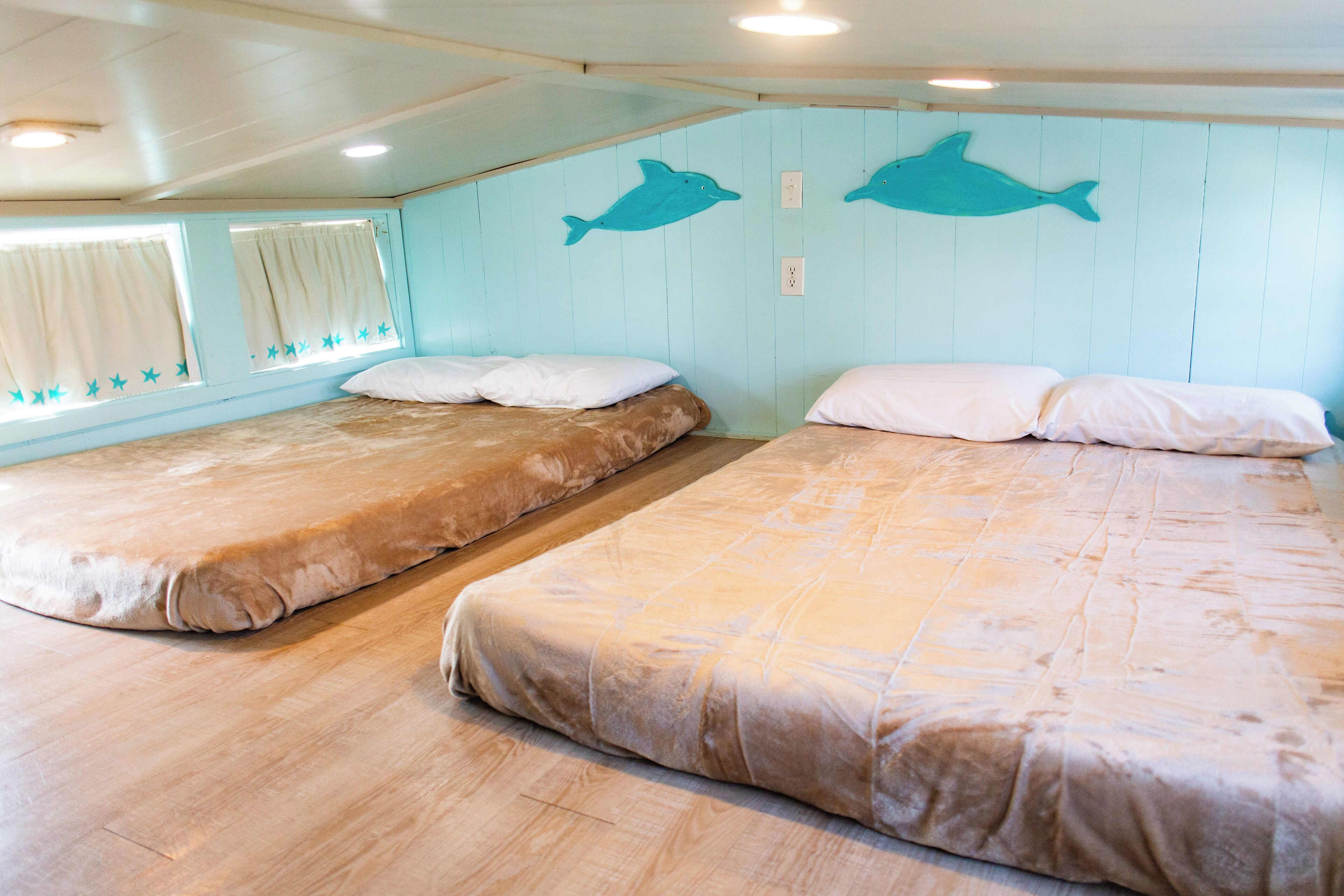 Ett rum med två sängar, ett fönster med gardiner och två väggdekaler med delfinmotiv.
