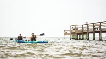 Dos personas en kayak sobre el agua, con un muelle de madera al fondo.