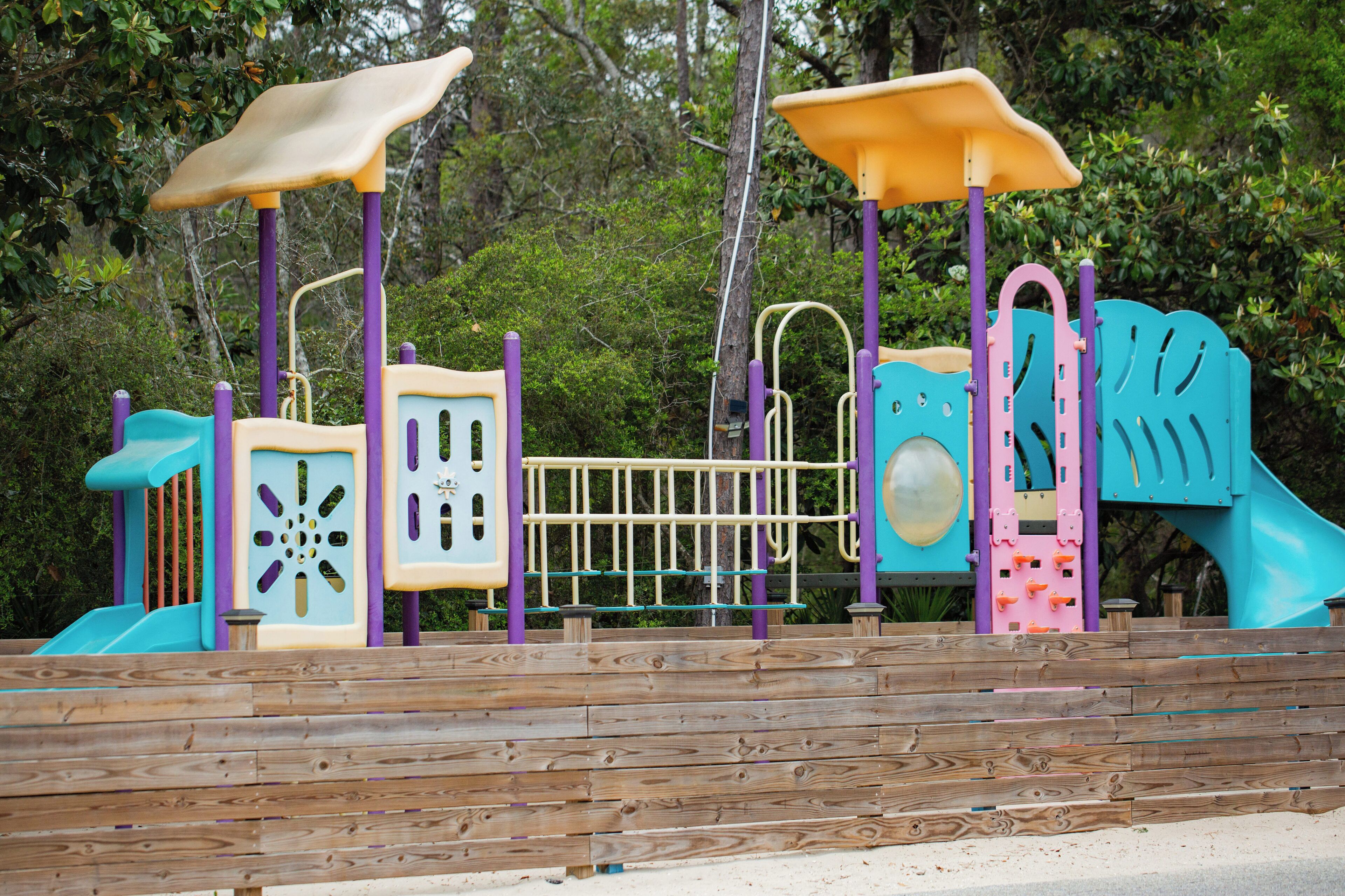 A wooden deck with a playground structure featuring slides, climbing areas, and a small enclosed space.