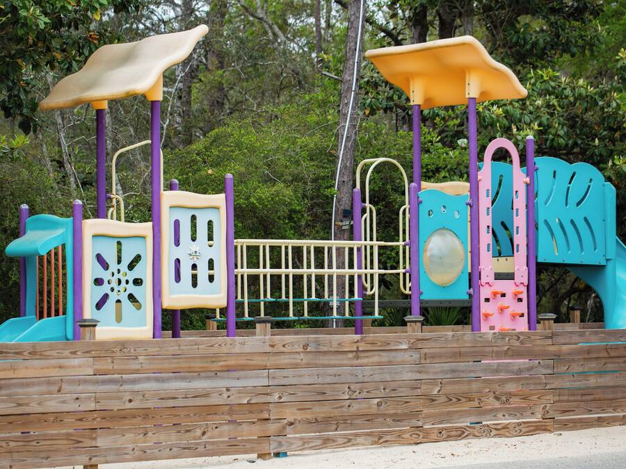 Una terraza de madera con un parque infantil que incluye toboganes, zonas de escalada y un espacio pequeño cerrado.
