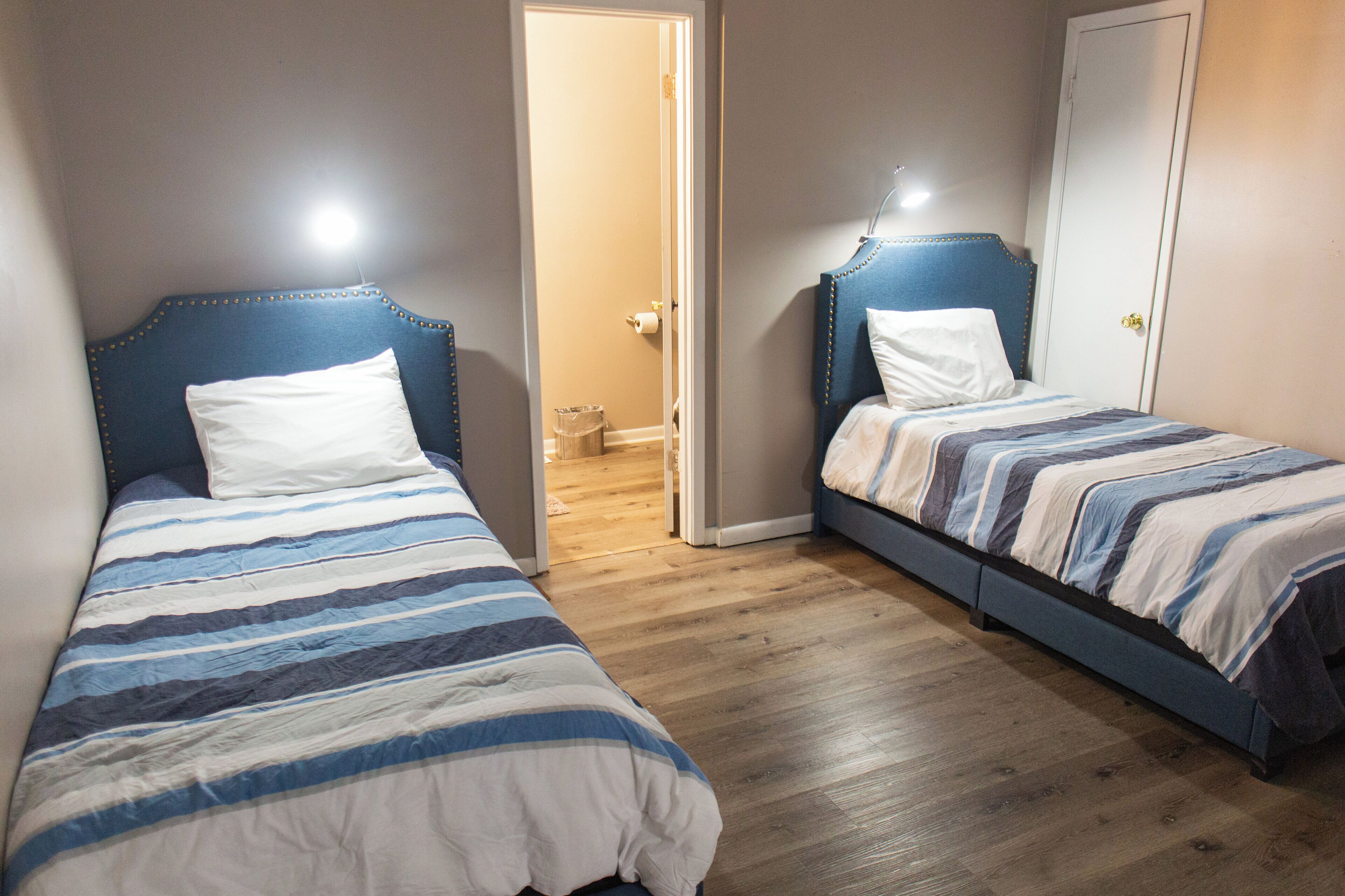 A bedroom with two beds, wooden flooring, and a door leading to a bathroom.