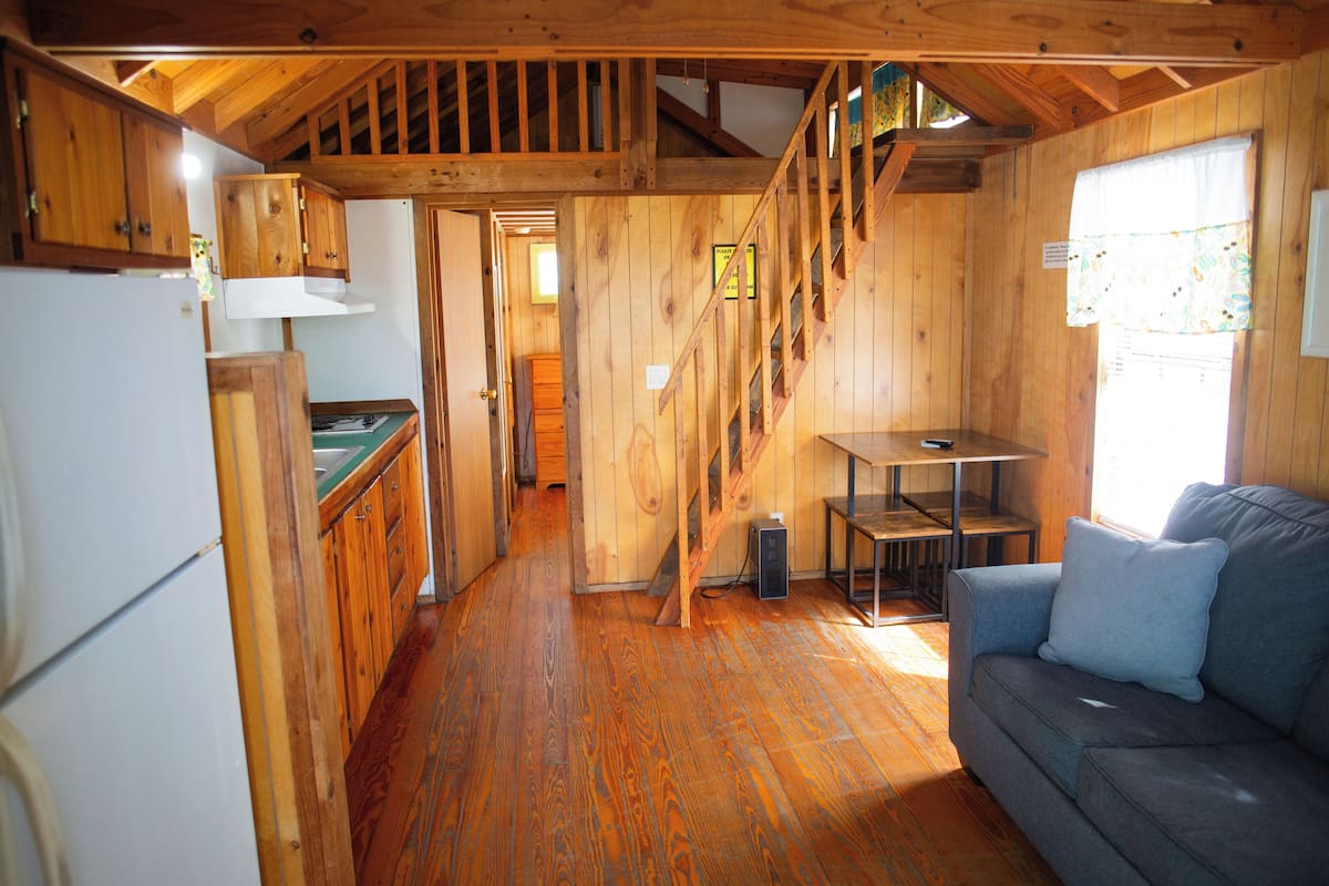 L’intérieur d’une cabane en bois comprend une cuisine, un coin repas et un escalier.