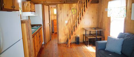 A wooden cabin interior with a kitchen, dining area, and a staircase.