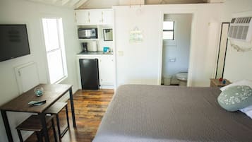 A bedroom with a bed, a desk, and a kitchenette.