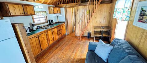 Un intérieur de chalet chaleureux avec un plancher en bois, un coin cuisine, un espace repas et un canapé.