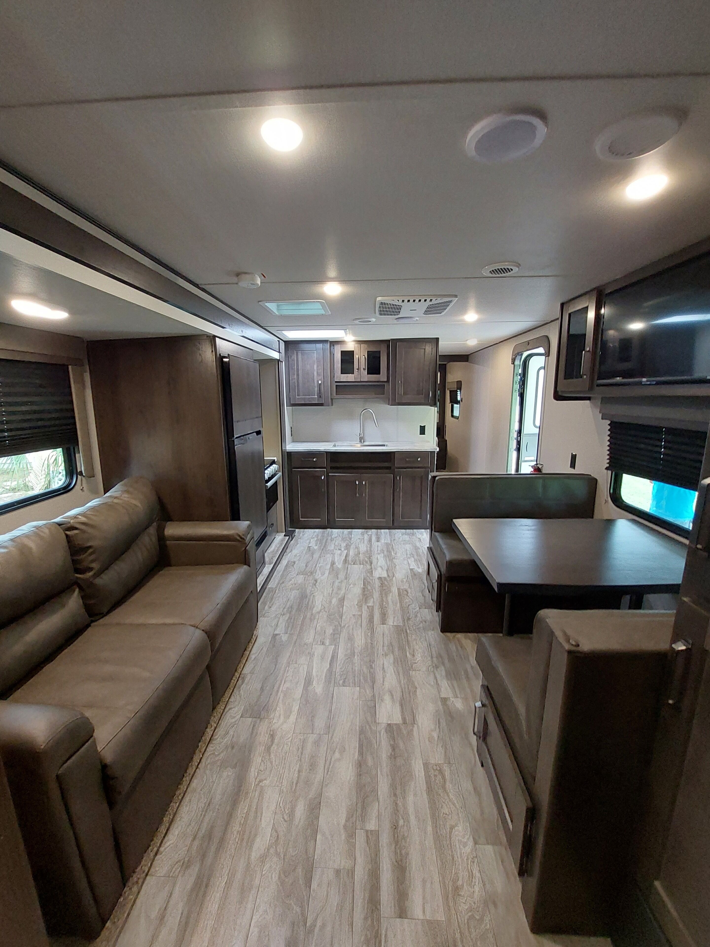A compact RV interior with a kitchenette, a sofa, a table, and a TV.