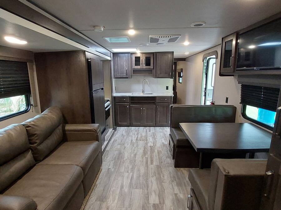 A compact RV interior with a kitchenette, a sofa, a table, and a TV.