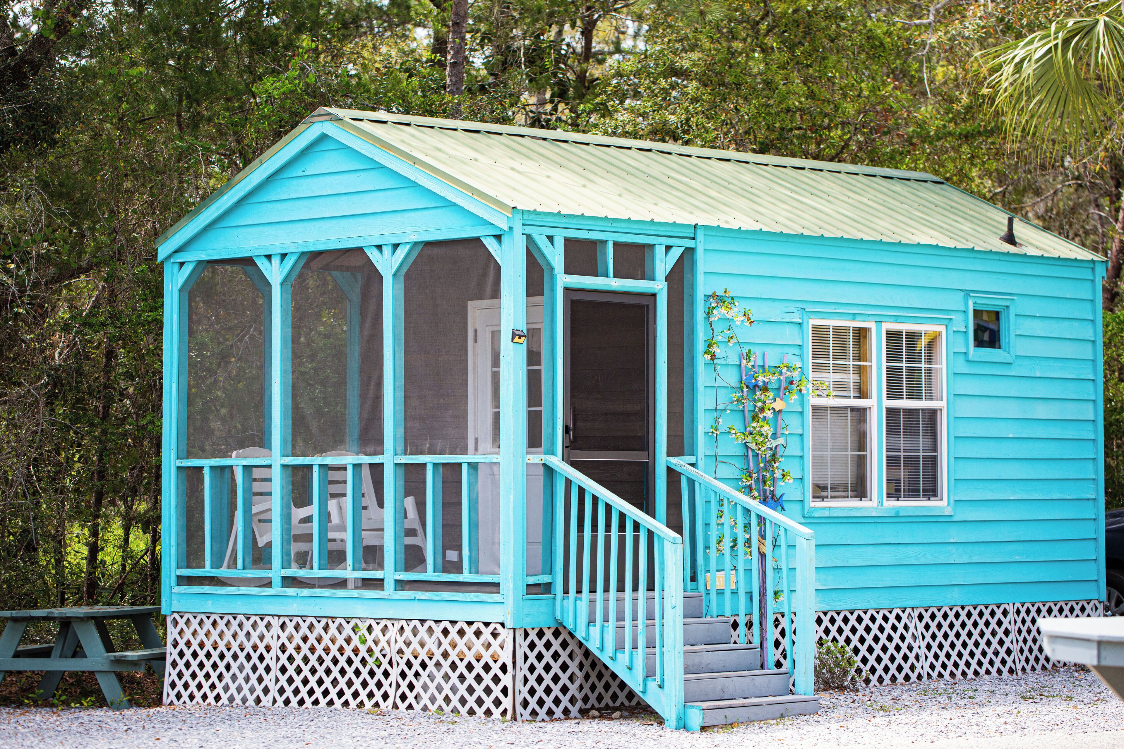 Une cabane en bois turquoise, dotée d’un porche, d’un escalier et d’une clôture à treillis.