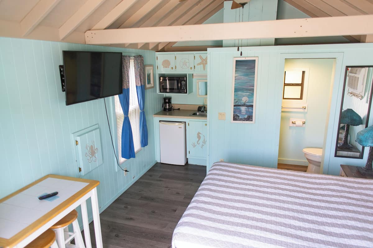 Une chambre de taille réduite comprenant un lit, une petite table, un téléviseur, une kitchenette et une salle de bain.