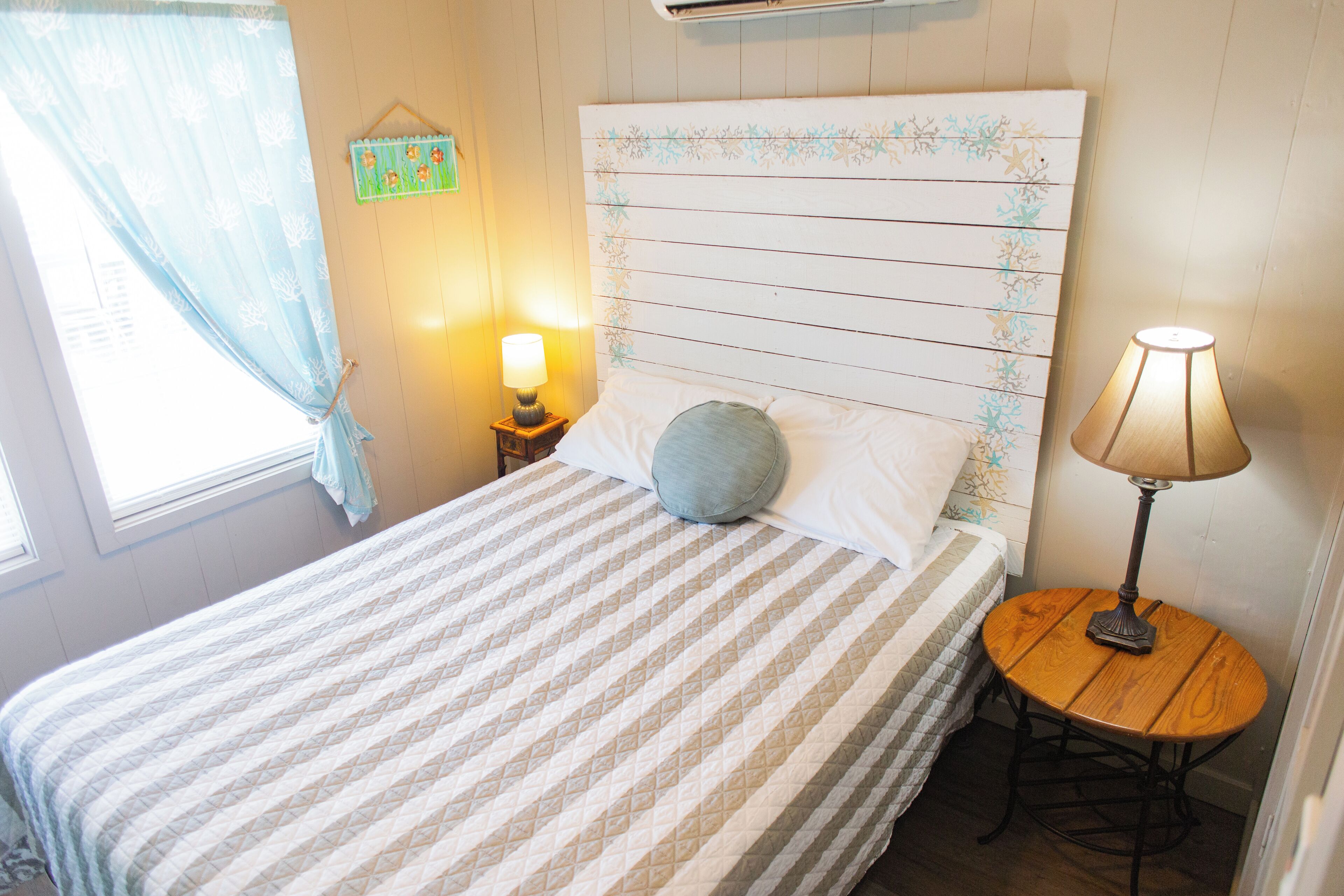 A bed with a striped bedspread, a headboard with floral patterns, a bedside lamp, and a small wooden table.