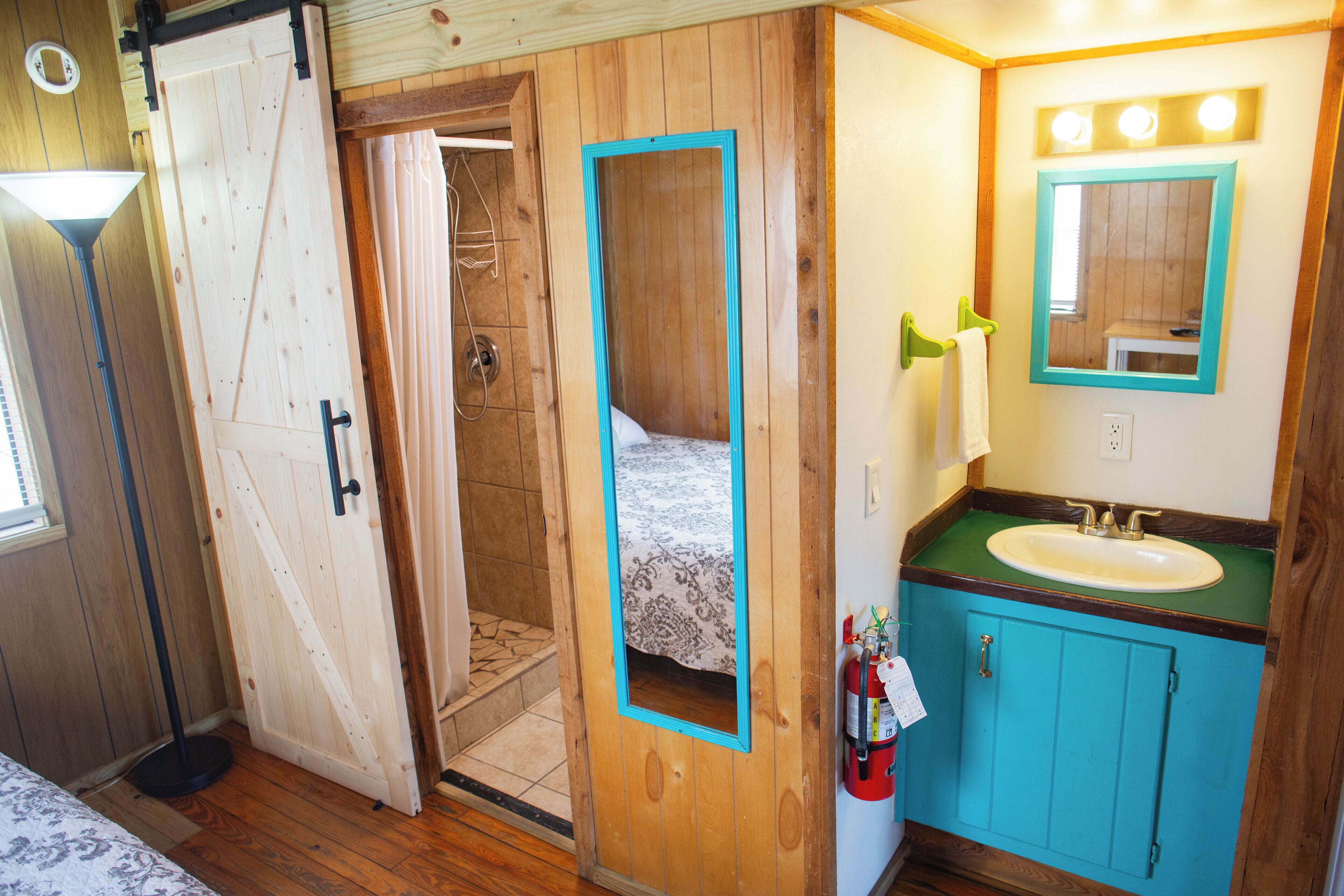 Ein Badezimmer mit Holztür, Waschbecken mit Spiegel und einem Handtuch, das an der Wand hängt.