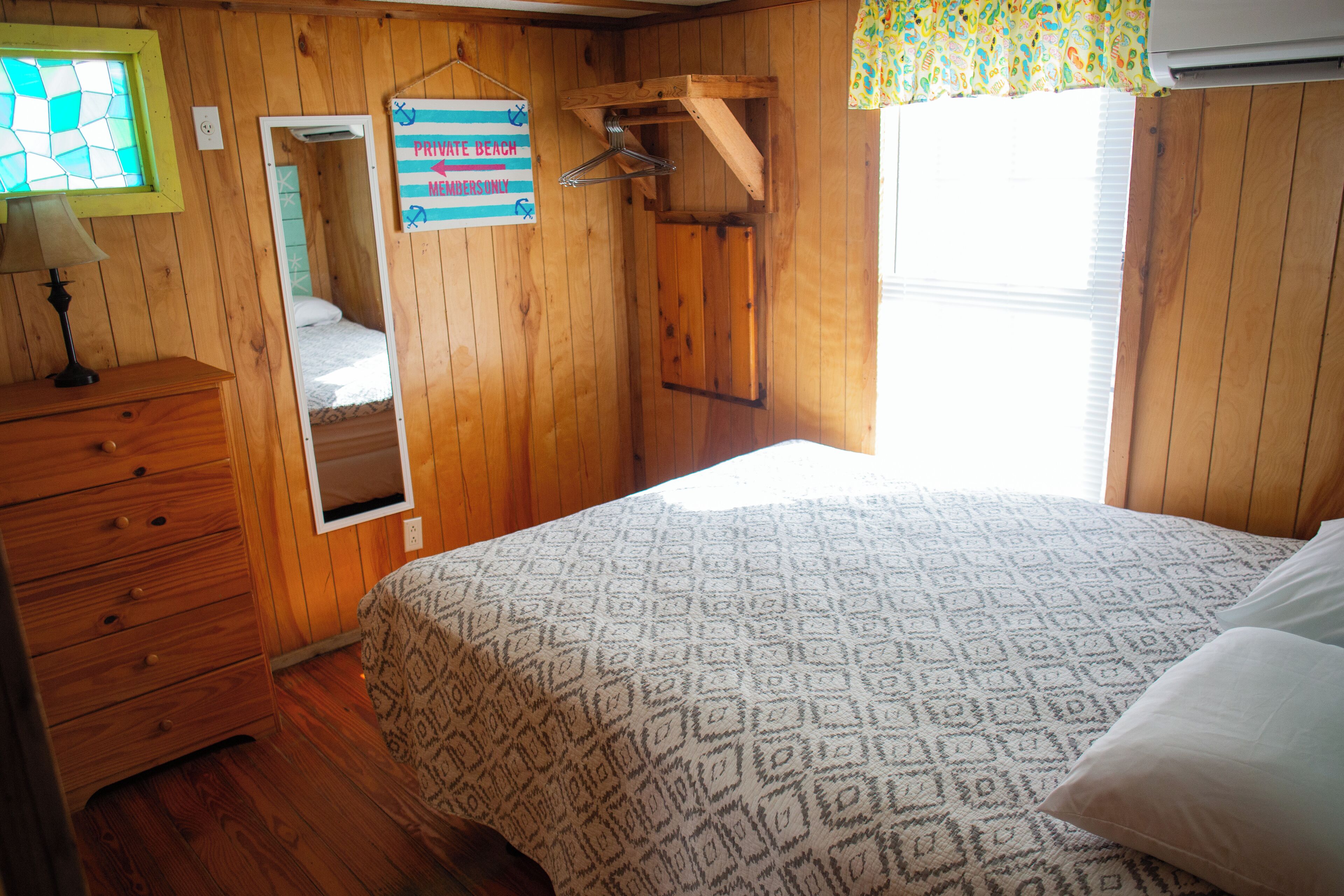A wooden room with a bed, a dresser, a mirror, and a sign indicating a private beach and a netted area.