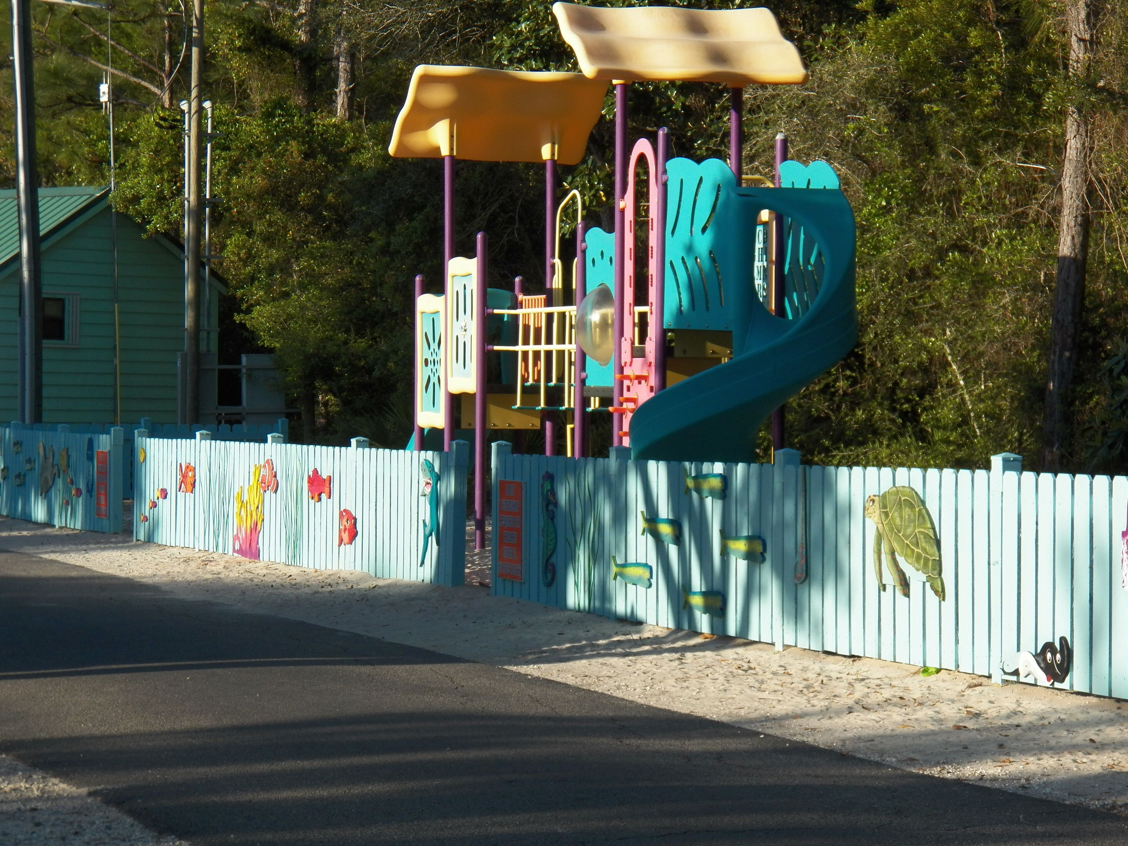 A playground with colorful equipment and a fence decorated with fish and sea creature cutouts.