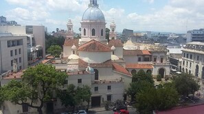 Un edificio histórico con una cúpula destacada y torres de campanas, rodeado de edificios modernos y árboles.