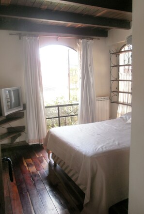 A bedroom with a bed, a television on a shelf, a window with curtains, and a balcony with a railing. - COLONIAL HOUSE IN NEW AND OLD SALTA (Salta)