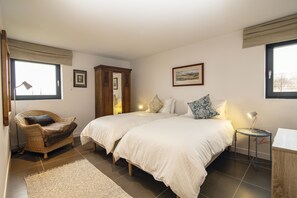 Quarto com duas camas, uma cadeira, uma mesinha e um armário.