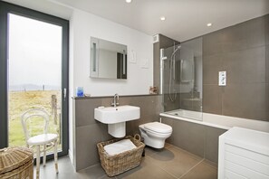 Casa de banho moderna com uma janela ampla, uma pia branca, sanita e cabine de duche com vidro.