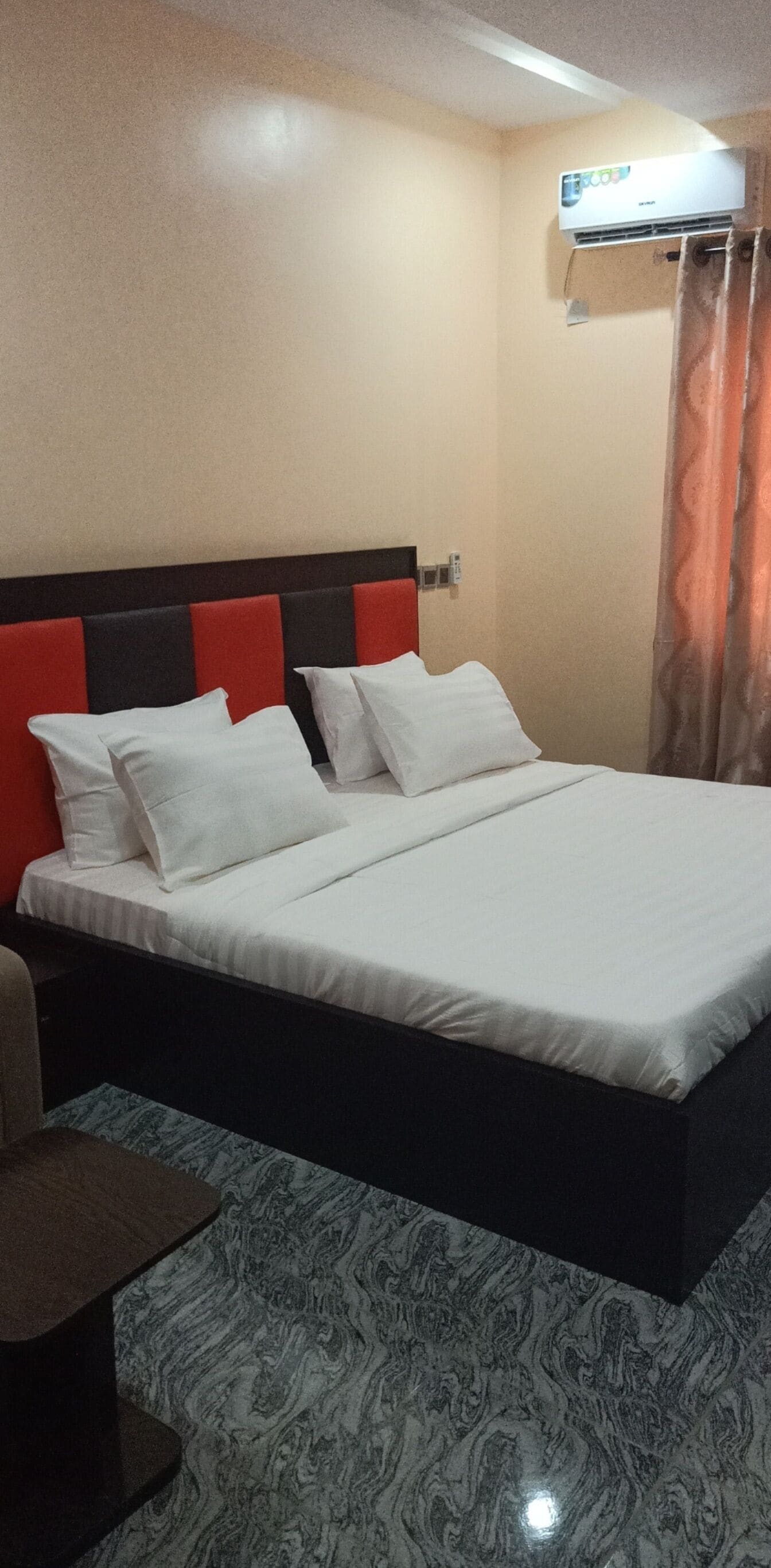 Quarto de hotel com cama, mesa de cabeceira, ar condicionado fixado na parede e cortina.