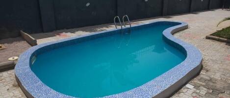 A rectangular swimming pool with a tiled edge, surrounded by a paved patio area.