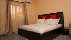 Un dormitorio con cama, cortinas, un equipo de aire acondicionado y una mesita de noche.