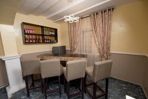Un comedor con una mesa redonda, cuatro sillas, una vinoteca con botellas y una araña.